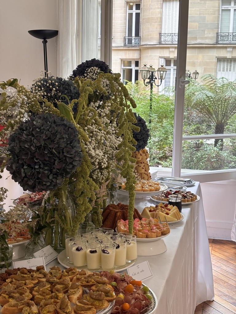 Buffet traiteur Rosy Paris fleuri dressé devant une fenêtre parisienne